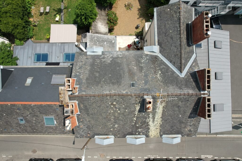 Avant : toiture d’immeuble angevin en ardoise, lichens jaunes sur noues et cheminées